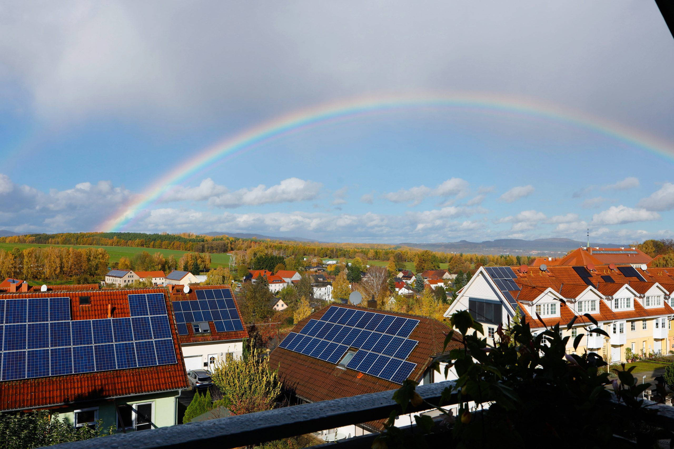 Häuser mit PV-Anlagen auf Dächern über die ein Regenbogen ist